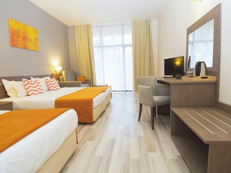 Bright hotel room with two beds, orange accents, and desk with mirror.