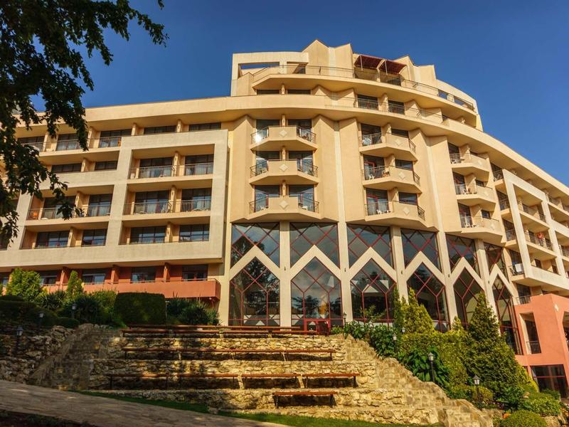 Multi-story hotel building with balconies and forecourt under clear sky.