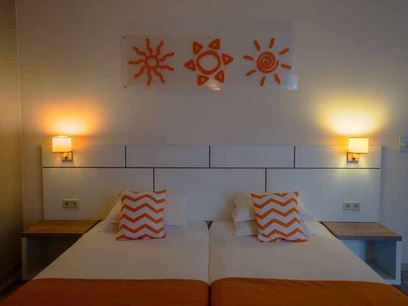 Twin room with two single beds, orange accents, and three sun paintings on the wall.