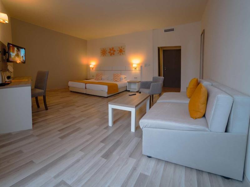 Spacious hotel room with double bed, sofa, desk, and wooden flooring.