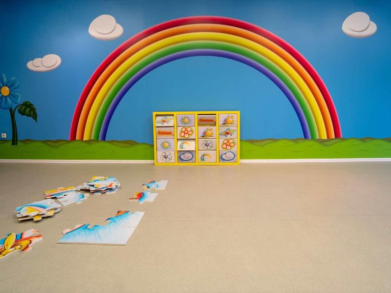 A colorful rainbow painted on a playroom wall with puzzles scattered on the floor.