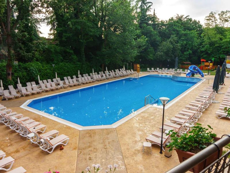 Large outdoor swimming pool with lounge chairs and greenery surrounded by trees.