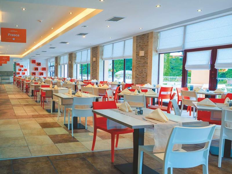 Modern, bright hotel restaurant with white and red chairs and large windows.