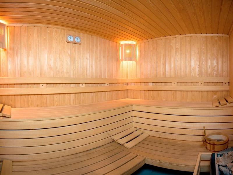 Interior of a sauna with wooden benches and wood paneling under warm lighting.