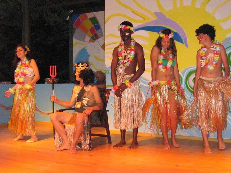 Five people in tropical costumes with flowers and grass skirts on a stage.