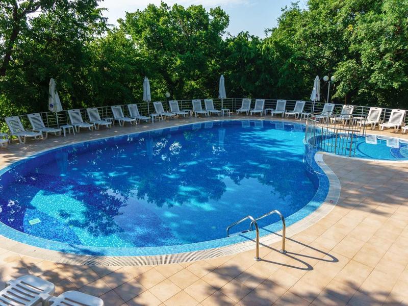 Large round outdoor pool with sun umbrellas and lounge chairs, surrounded by trees.