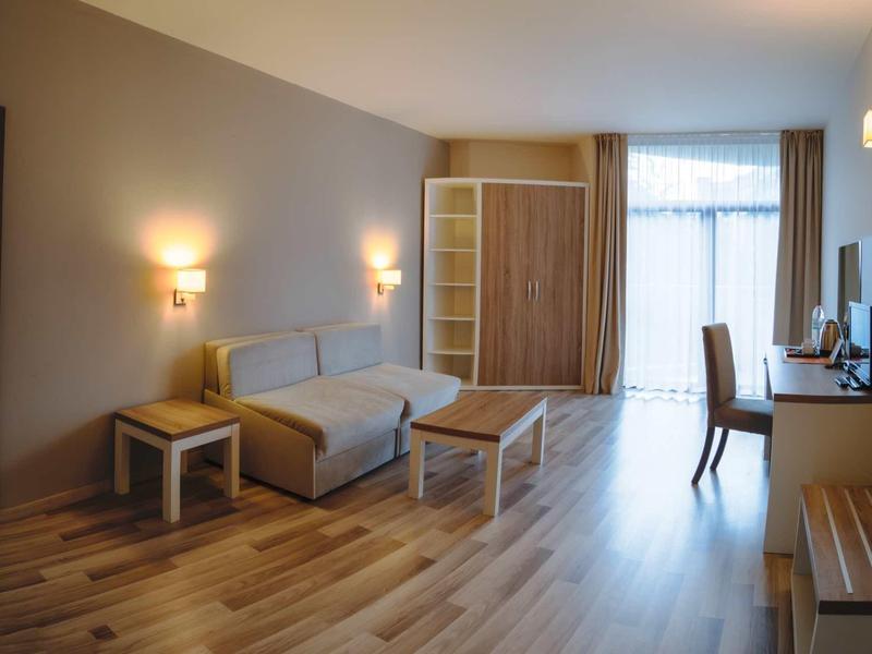 Bright hotel room with sofa, wooden tables, wardrobe, and desk by the window