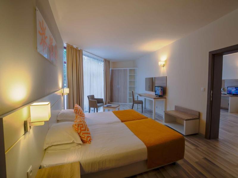 Modernly furnished hotel room with double bed, TV, and access to an adjoining room.