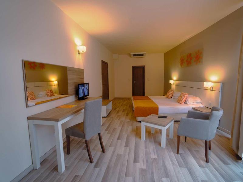 Bright hotel room with double bed, desk, chairs, and large mirror.