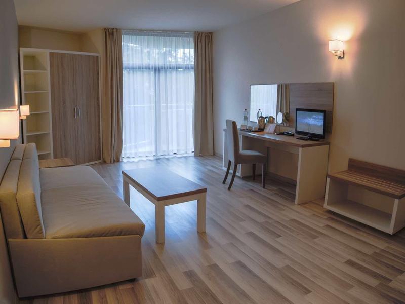 Bright hotel room with sofa, coffee machine, desk, and TV.