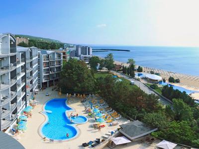 Hôtel avec piscine, transats, espaces verts et plage avec vue sur la mer.