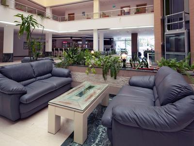 Salon d'hôtel moderne avec canapés en cuir bleus et table basse en verre près de plantes vertes.