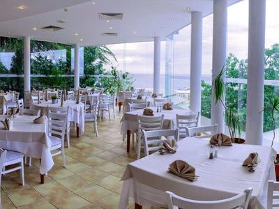 Restaurant lumineux avec tables et chaises blanches et vue sur la mer à travers de grandes fenêtres.