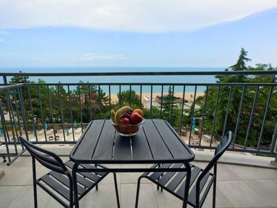 Balcon avec table et chaises, bol de fruits, vue sur la mer et la plage.
