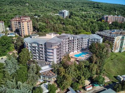 Complexe hôtelier moderne avec piscine, entouré d'arbres et proche d'une colline boisée.