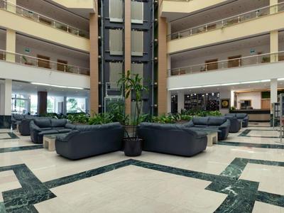 Grande hall d'hôtel moderne avec espaces de sièges, plantes et balcons à plusieurs niveaux.