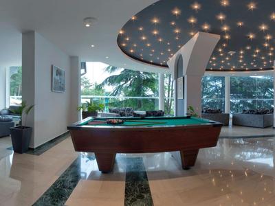 Jasna lobby hotelowa z bilardem, sofami i dużymi oknami z widokiem na ogród