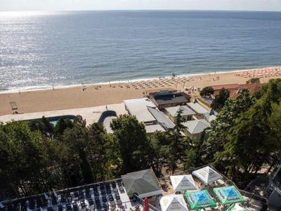 Vue sur une piscine avec des transats, la plage et la mer sous un ciel dégagé.