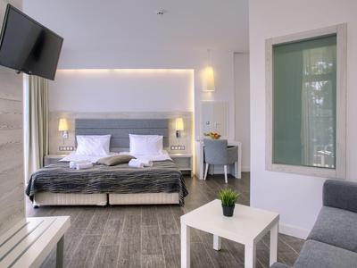 Chambre d'hôtel moderne avec lit double confortable, coin salon et TV murale.