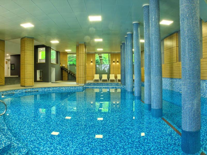 Piscine intérieure avec carreaux bleus, colonnes et grandes fenêtres dans un hôtel moderne