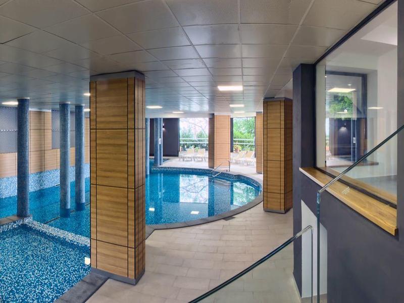 Piscine intérieure moderne avec espaces de détente et murs en verre dans un hôtel élégant.