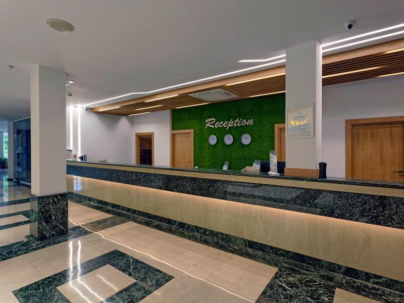 Réception d'hôtel moderne avec panneaux en marbre foncé et mur vert avec inscription.