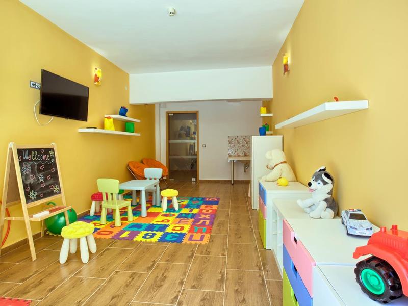 Salle de jeux colorée avec mobilier enfant, jouets et tapis éducatif dans une zone d'hôtel.
