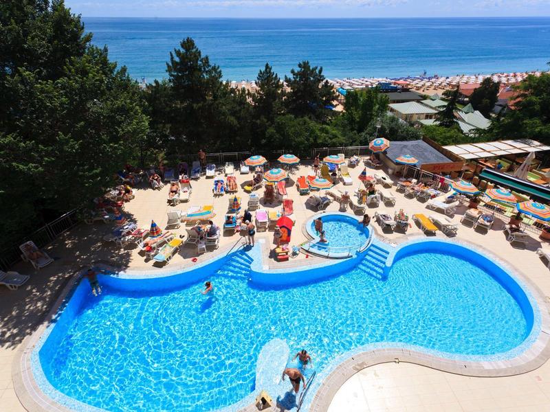 Piscine extérieure avec parasols et invités près des arbres et de la mer en arrière-plan