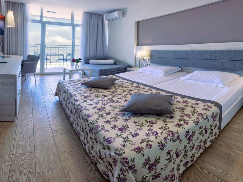 Chambre d'hôtel lumineuse avec grand lit, télévision et balcon avec vue sur la mer.