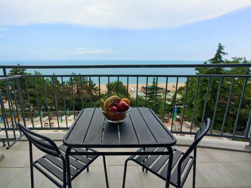 Balcon avec table et chaises, bol de fruits, vue sur la mer et la plage.