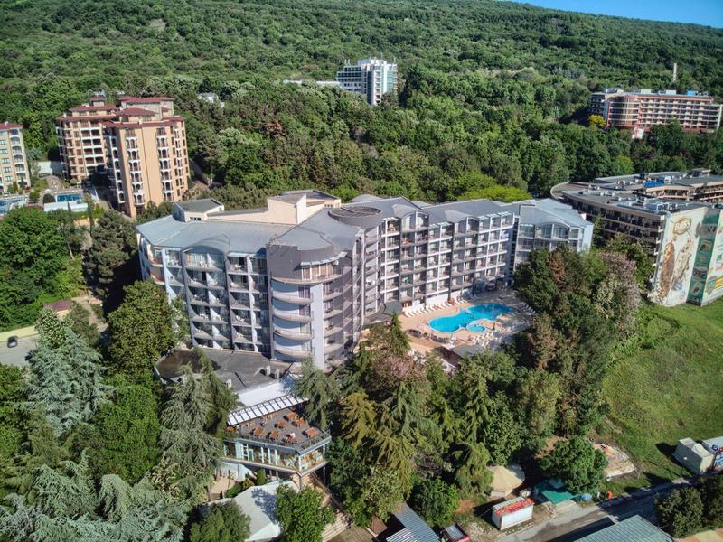 Complexe hôtelier moderne avec piscine, entouré d'arbres et proche d'une colline boisée.