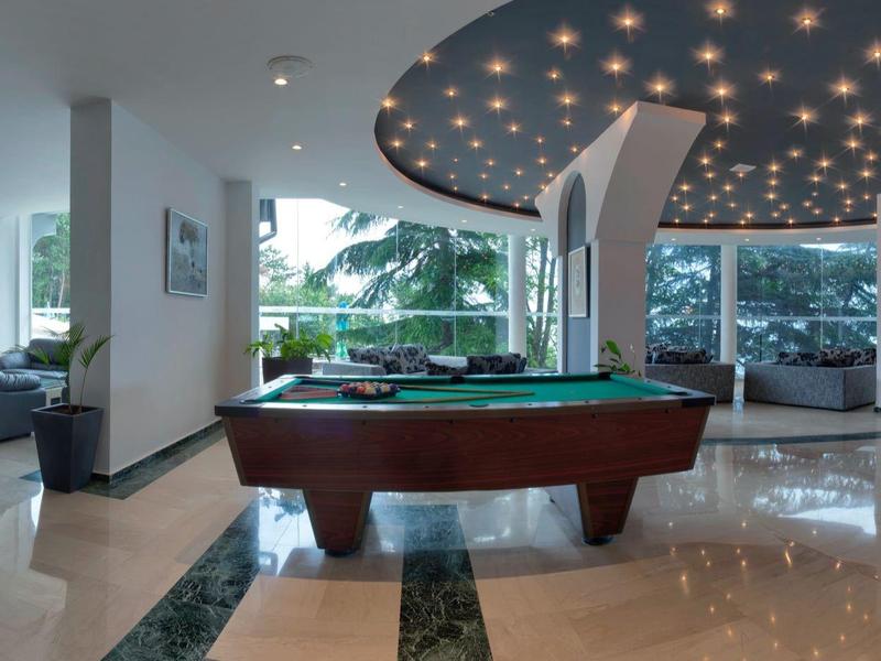 Espace hôtelier moderne avec table de billard, coins salons confortables et grandes fenêtres donnant sur un jardin.