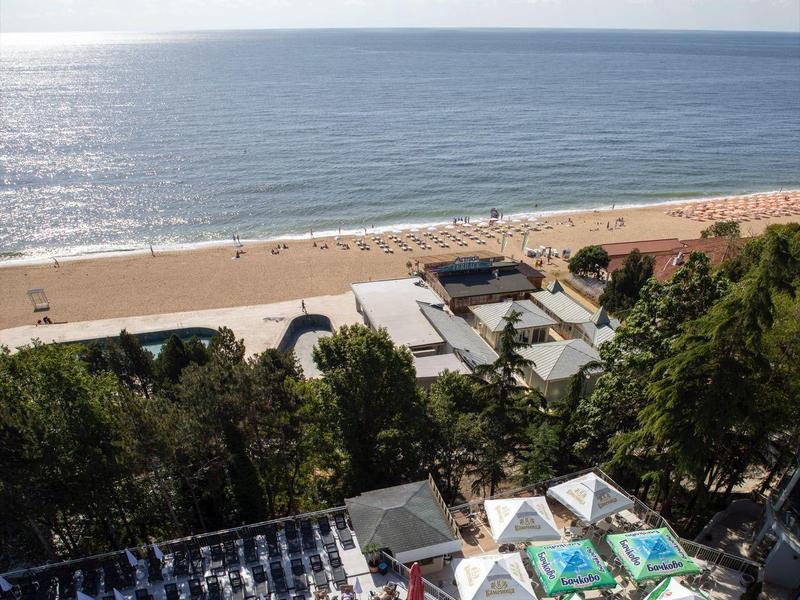Vue sur une piscine avec des transats, la plage et la mer sous un ciel dégagé.