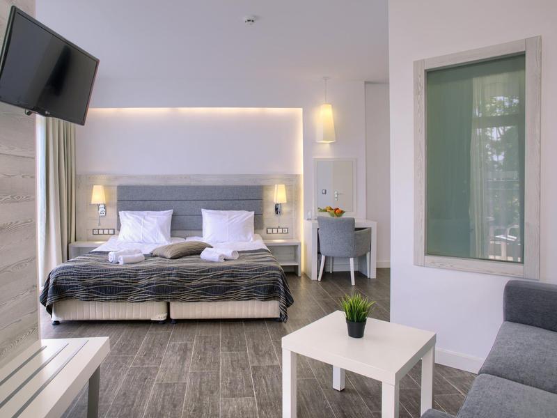 Chambre d'hôtel moderne avec lit double confortable, coin salon et TV murale.