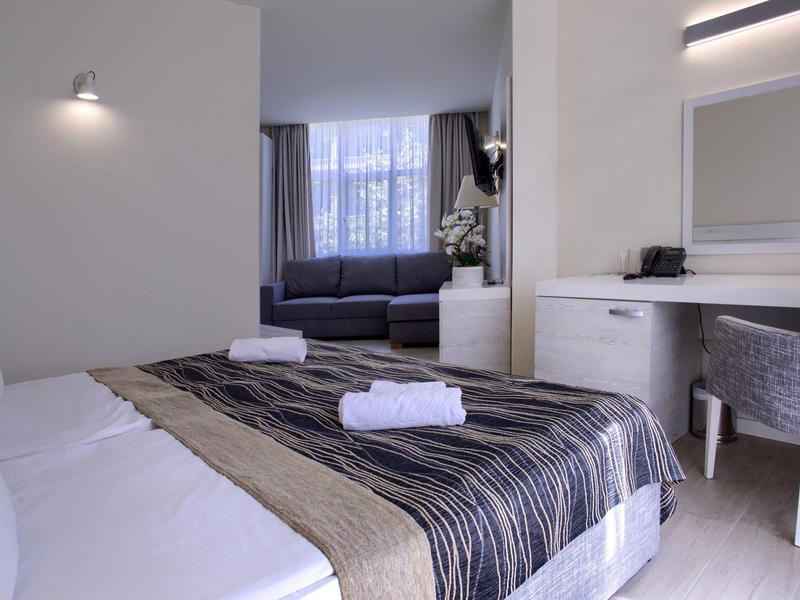 Chambre d'hôtel moderne avec lit, bureau, miroir et fenêtre avec rideaux.