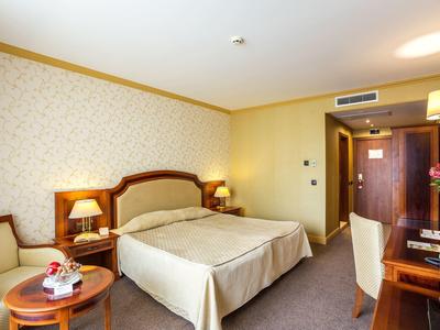 Camera d'hotel accogliente con letto matrimoniale, comodini, tavolo e sedie, luminosa e invitante.