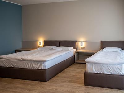 Camera d'hotel arredata semplicemente con letto matrimoniale, letto singolo e pavimento in legno.