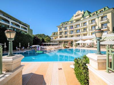Hotel con grande piscina esterna, ombrelloni e sdraio sotto un cielo limpido.