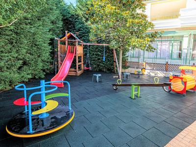 Colorato parco giochi per bambini con scivolo, struttura da arrampicata, giostra e altalena vicino a un edificio.