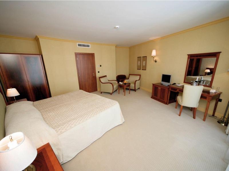 Camera d'hotel spaziosa con due letti, tavolo, sedie e scrivania con specchio.