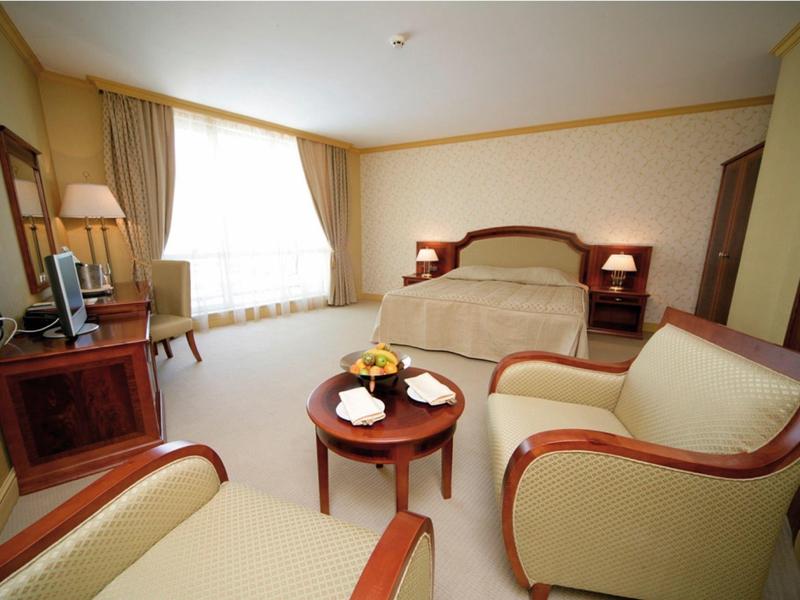 Camera d'hotel luminosa con letto matrimoniale, due poltrone e un piccolo tavolo rotondo.