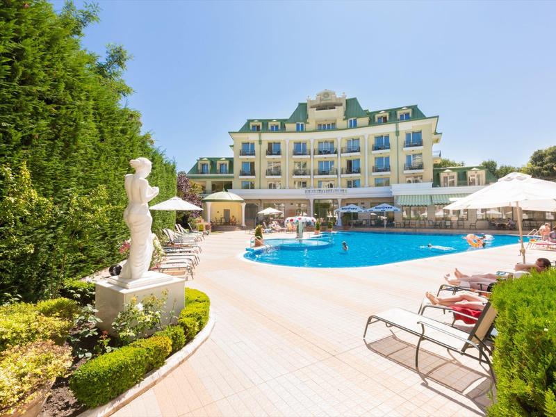 Hotel di lusso con grande piscina all'aperto, ombrelloni e giardino verde sotto un cielo sereno.
