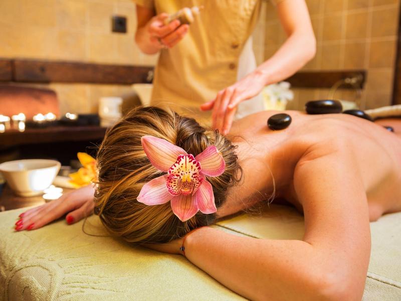Persona che riceve un massaggio con pietre calde con fiore nei capelli in una spa benessere.
