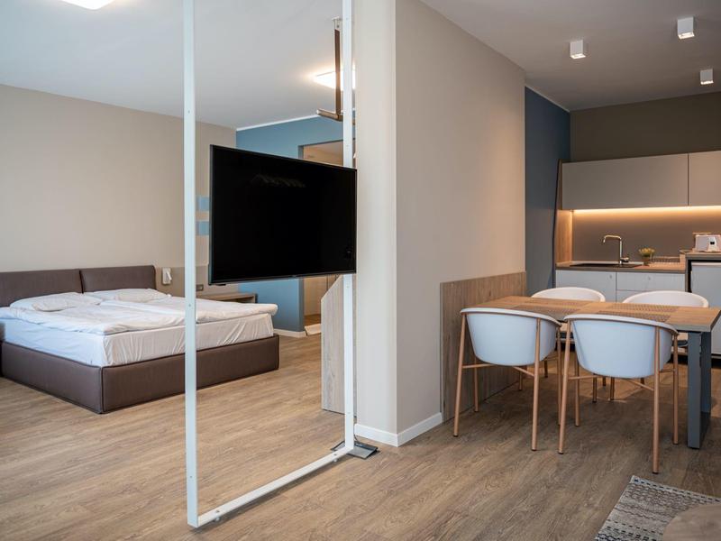 Camera d'hotel moderna con letto matrimoniale, TV a parete e zona pranzo con quattro sedie.