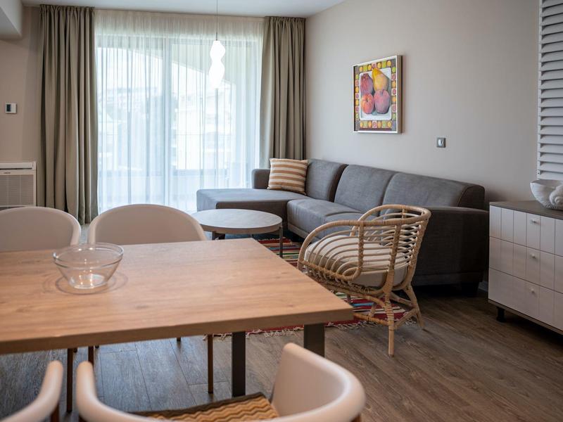 Soggiorno moderno con divano, sedia in rattan e tavolo in legno chiaro.