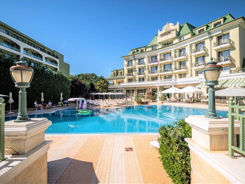 Hotel con grande piscina all'aperto, ombrelloni e lettini sotto un cielo azzurro sereno.