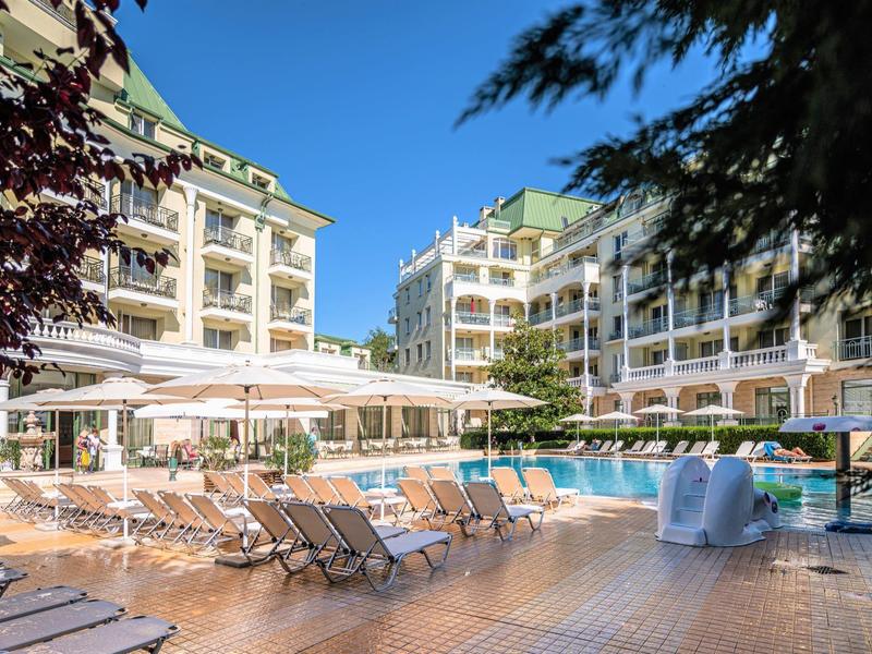 Piscina dell'hotel con lettini e ombrelloni davanti a un edificio multipiano sotto un cielo limpido.