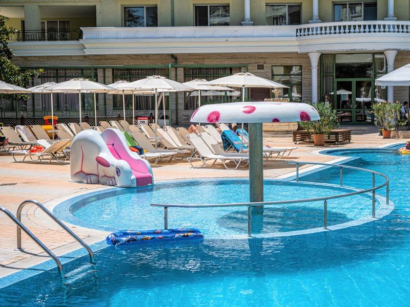 Piscina per bambini con spruzzo d'acqua a fungo colorato e scivolo accanto alla piscina esterna dell'hotel