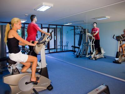 Mensen trainen op hometrainers voor een grote spiegel in een moderne fitnessruimte.