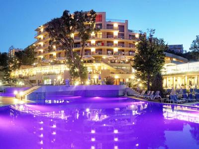 Luxe hotel met verlicht buitenzwembad 's nachts onder een heldere hemel.